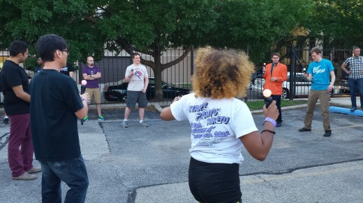 Adults on a concrete surface hold colored controllers in the air and move around.